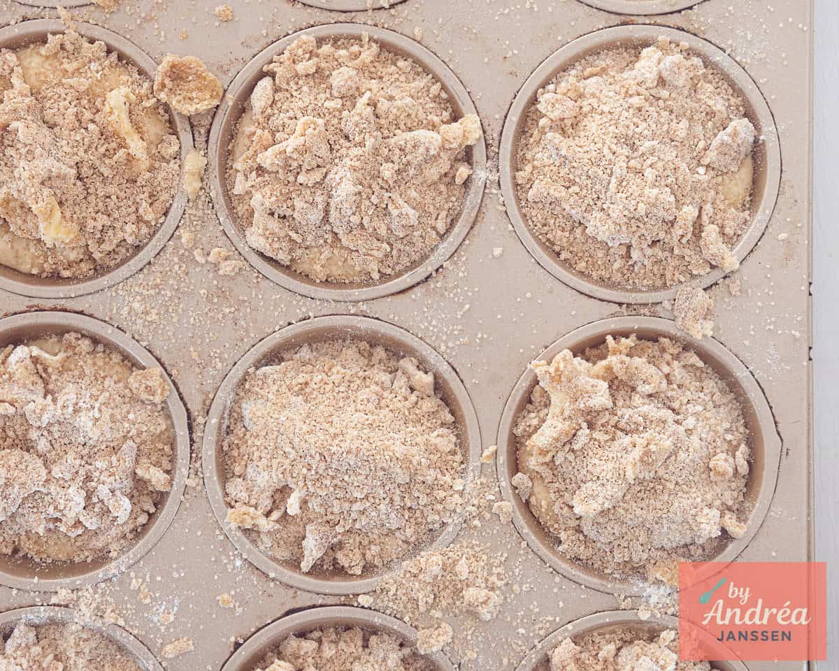 A muffin tin filled with batter and some streusel on top
