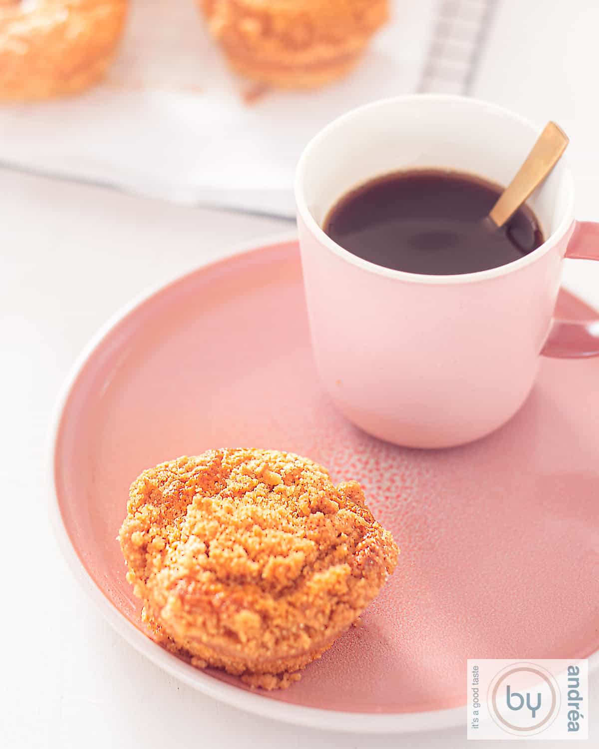 Een roze bord met een muffin met speculaas en kruimeltopping. Een kopje koffie staat erbij
