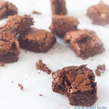 Homemade chocolate brownies on a white suface. The front one has taken a bite out.