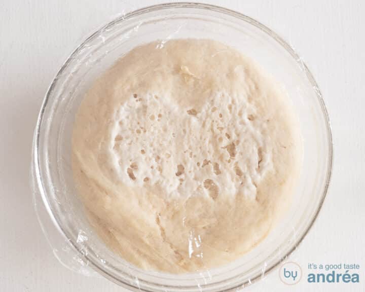 Risen dough in a glass bowl, covered with plastic wrap.