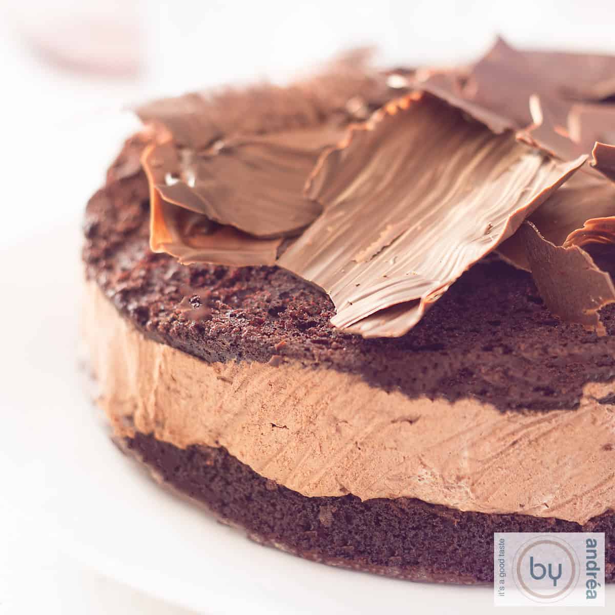 A square photo of a slice of a chocolate cake with mousse and chocolate flakes, homemade, on top. A white background.