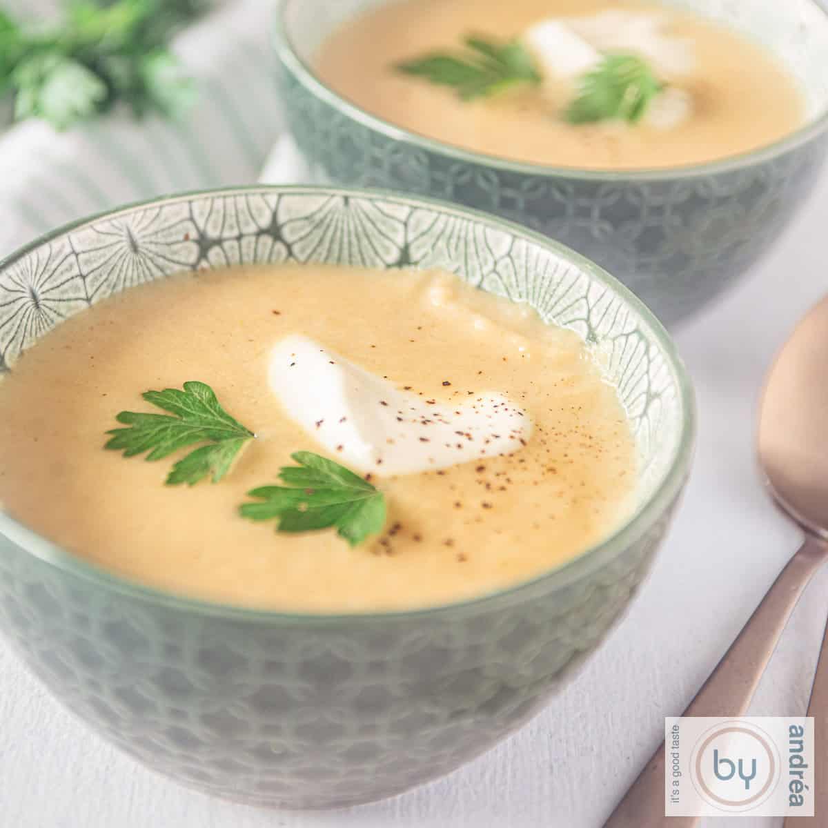 A square photo of two bowls of soup, filled with parsnip soup, cream and yoghurt.
