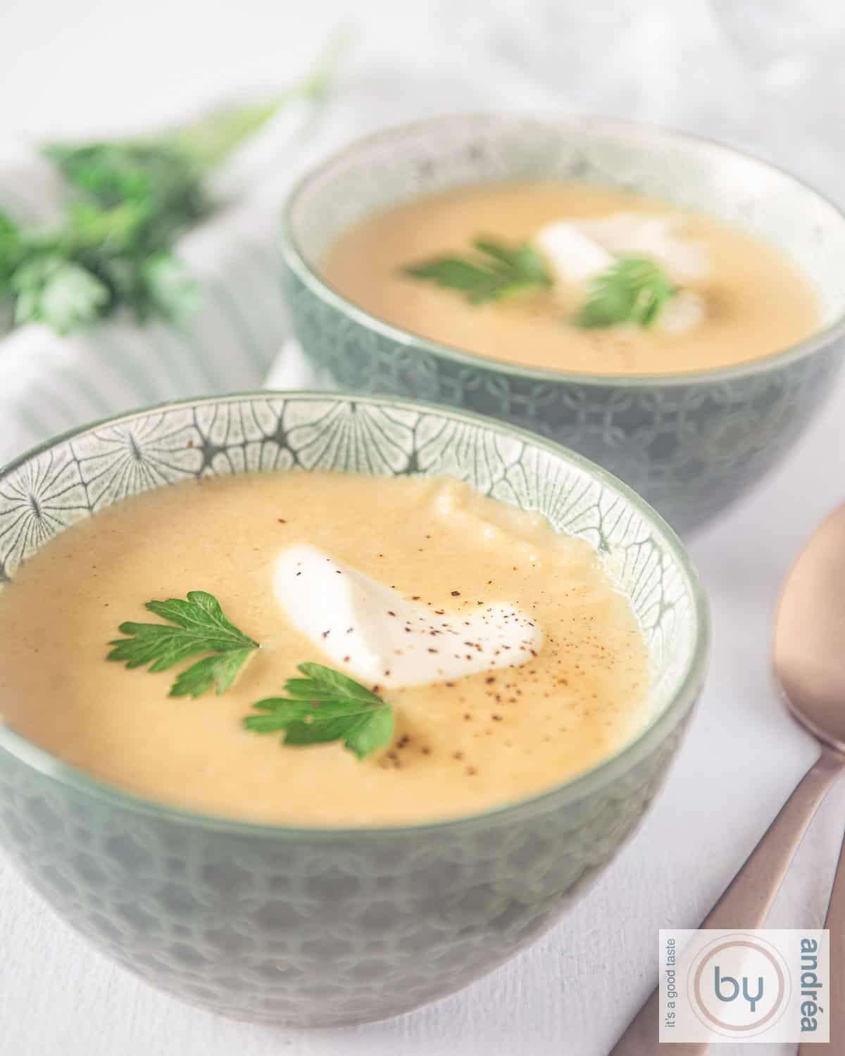 Een hoogtefoto met twee groene kommen gevuld met pastinaaksoep achter elkaar. Een garnering van yoghurt en koriander