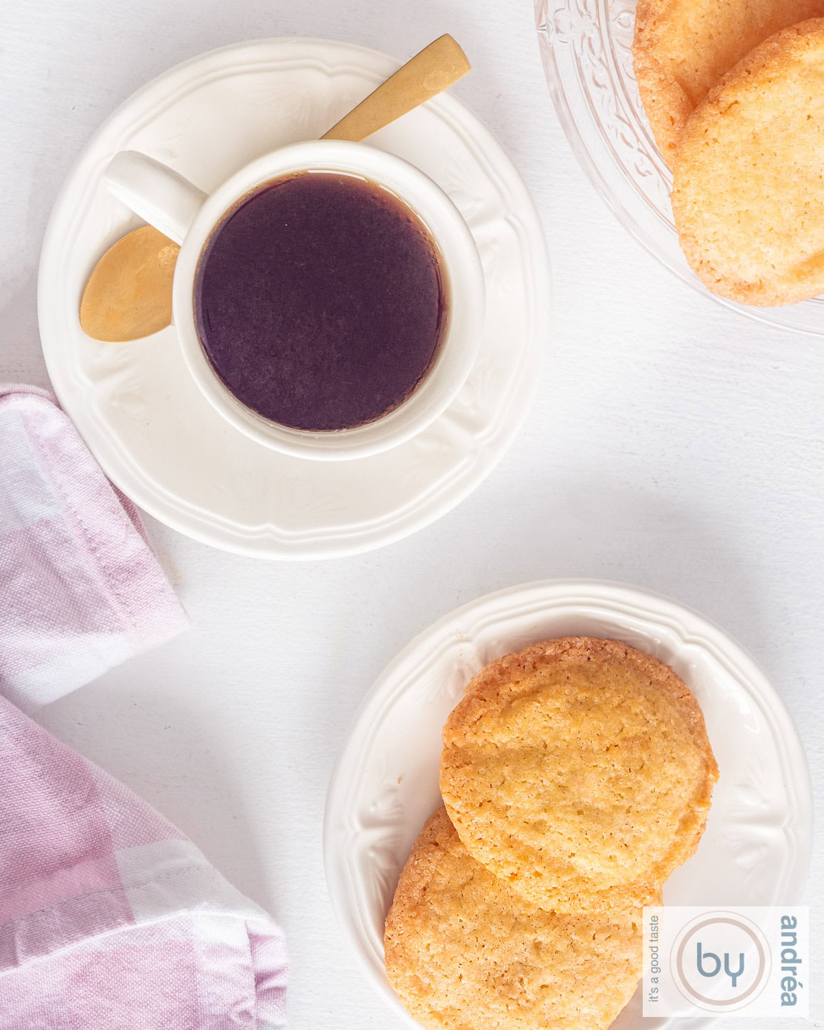 Een foto van bovenaf van een schaal met koekjes, twee zandkoekjes op een bord en een kopje koffie.
