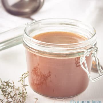 Jar with homemade beef stock on a white background. Some herbs laying in front.