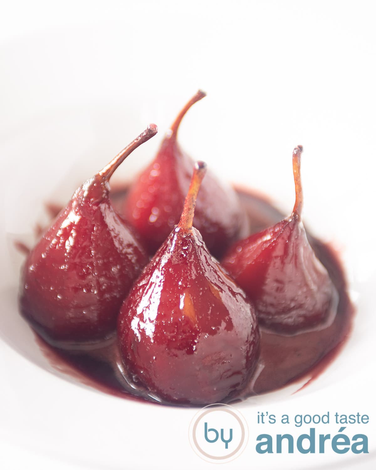 Four poached pears with poaching syrup in a white deep plate