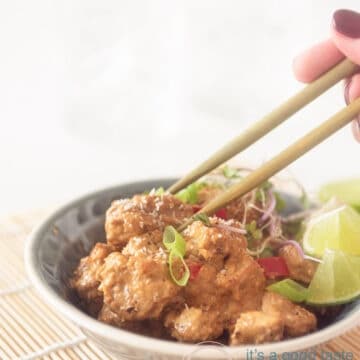 a grey bowl with diced pork in soy sauce. Two chopsticks are taking a bite.