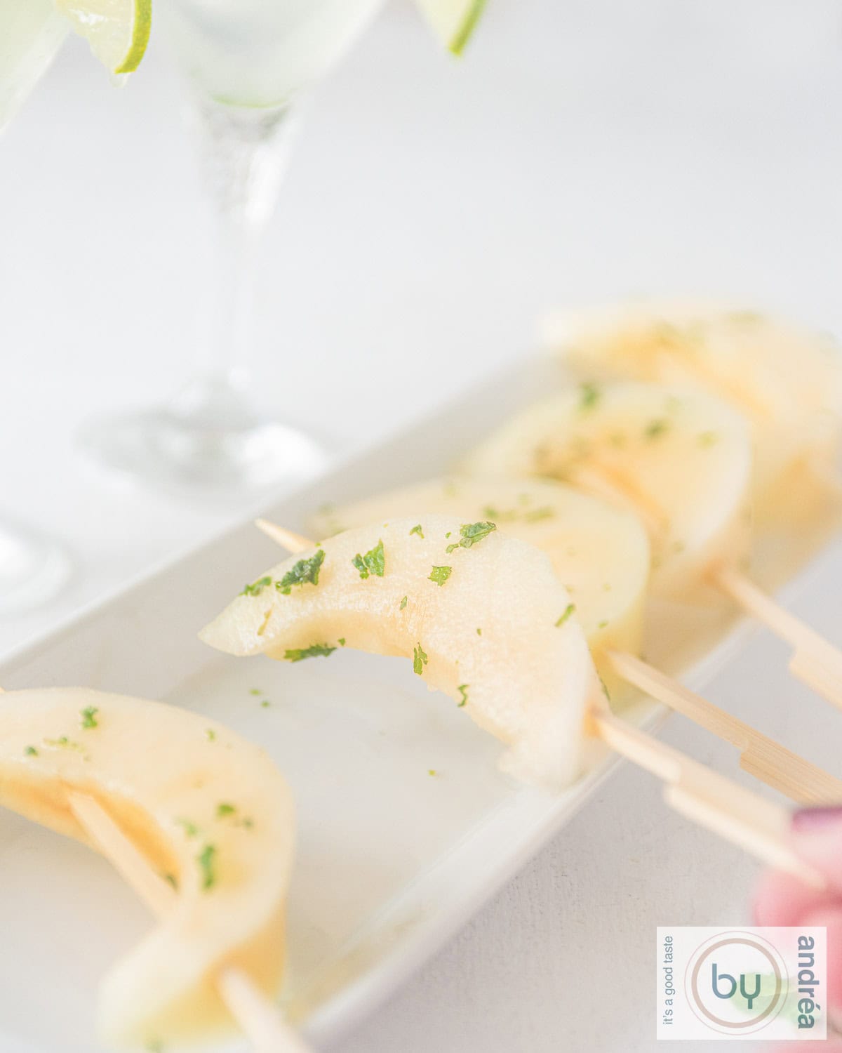 A white bowl holds five marinated Galia melon slices in a row, marinated in a mojito marinade. A hand grasps a slice.