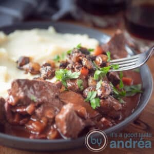 A square photo with a gray plate, mashed potatoes, French beef bourguignon with parsley.