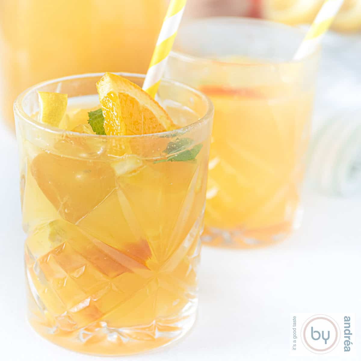 A square photo with two glasses of iced tea with lemon and mint in front of a carafe.