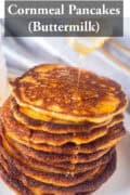 A pile of cornmeal pancakes on a white plate drizzled honey on top. A text: cornmeal pancakes (buttermilk)