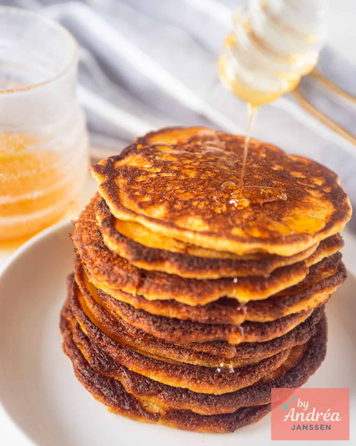 A white plate, a drizzle of honey on top of cornflour pancakes with buttermilk