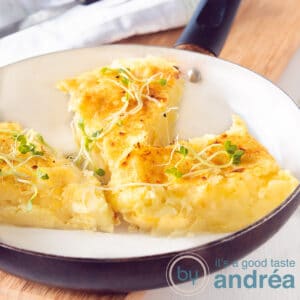 A square photo with a white frying pan with three potato tips with some greenery. Everything on a wooden board