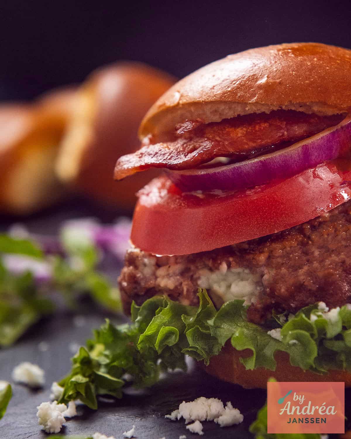 Een gestapeld broodje hamburger gevuld met feta en belegt met sla, tomaat, ui en bacon.