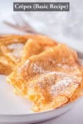 Half a white plate with crepes dusted with powdered sugar. A text on top: Crêpes (basic recipe)