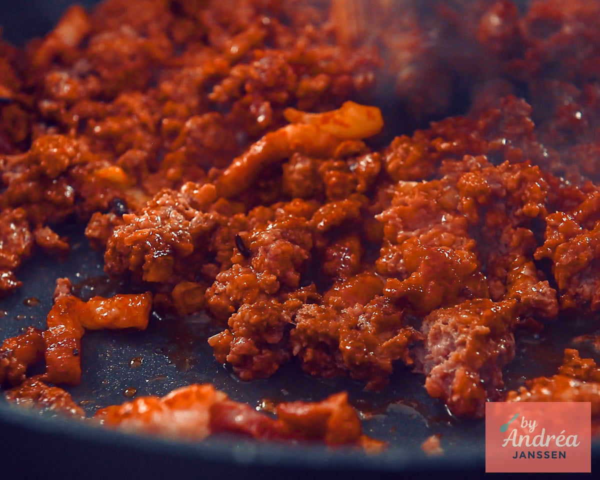 Ground beef and bacon pieces mixed with tomato paste in a skillet.