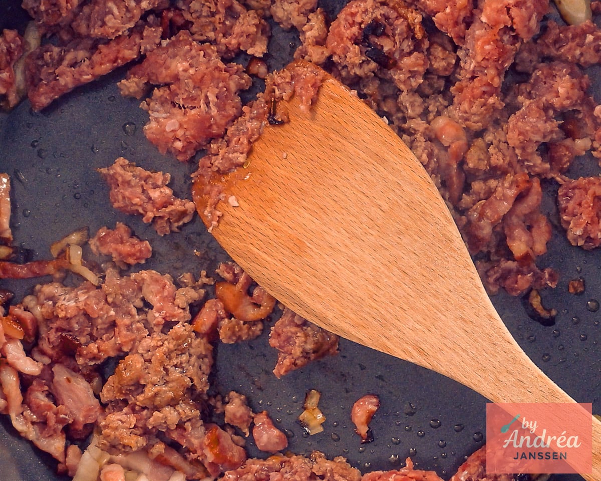 Gehakt en spekreepjes gemengd met tomatenpuree in een koekenpan.
