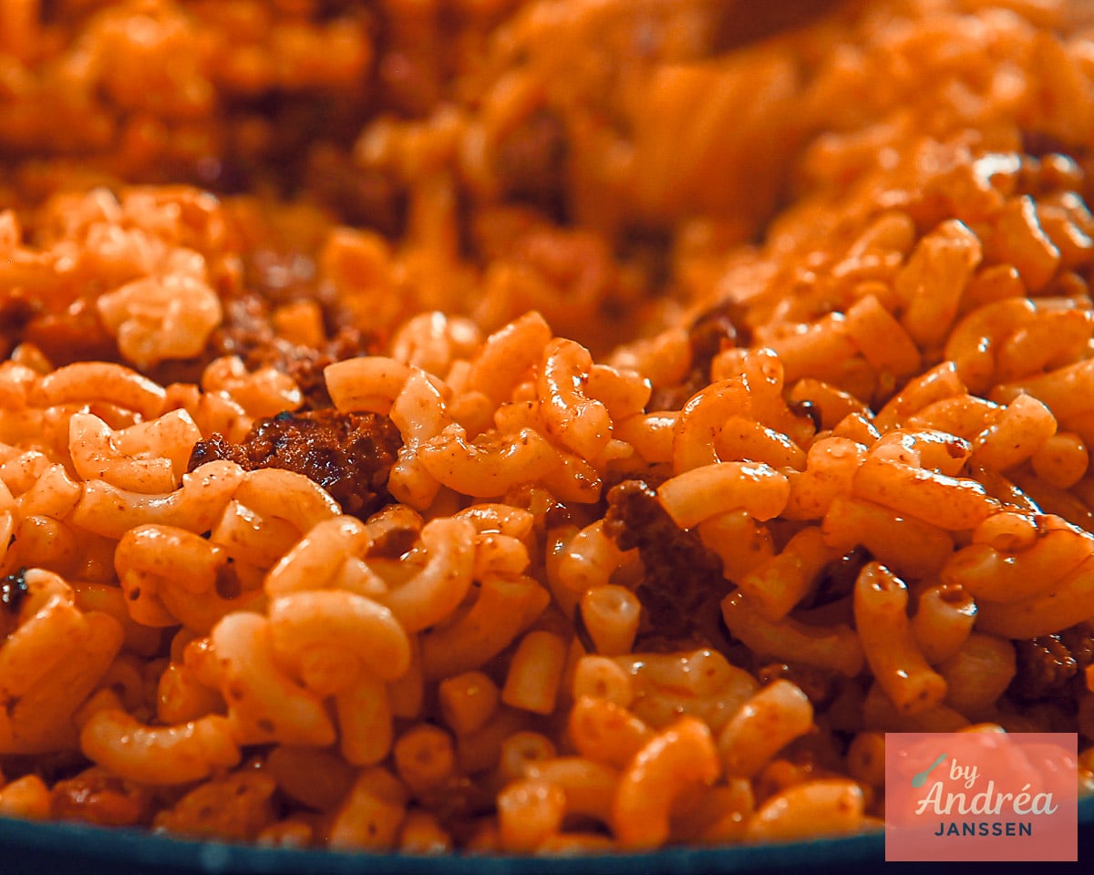 Close-up of elbow macaroni mixed with ground beef, bacon, and tomato paste in the pan.