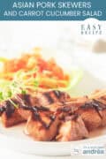 Three Pork loin skewers with salad on a white plate. Text: Asian pork skewers and carrot cucumber salad, easy recipe
