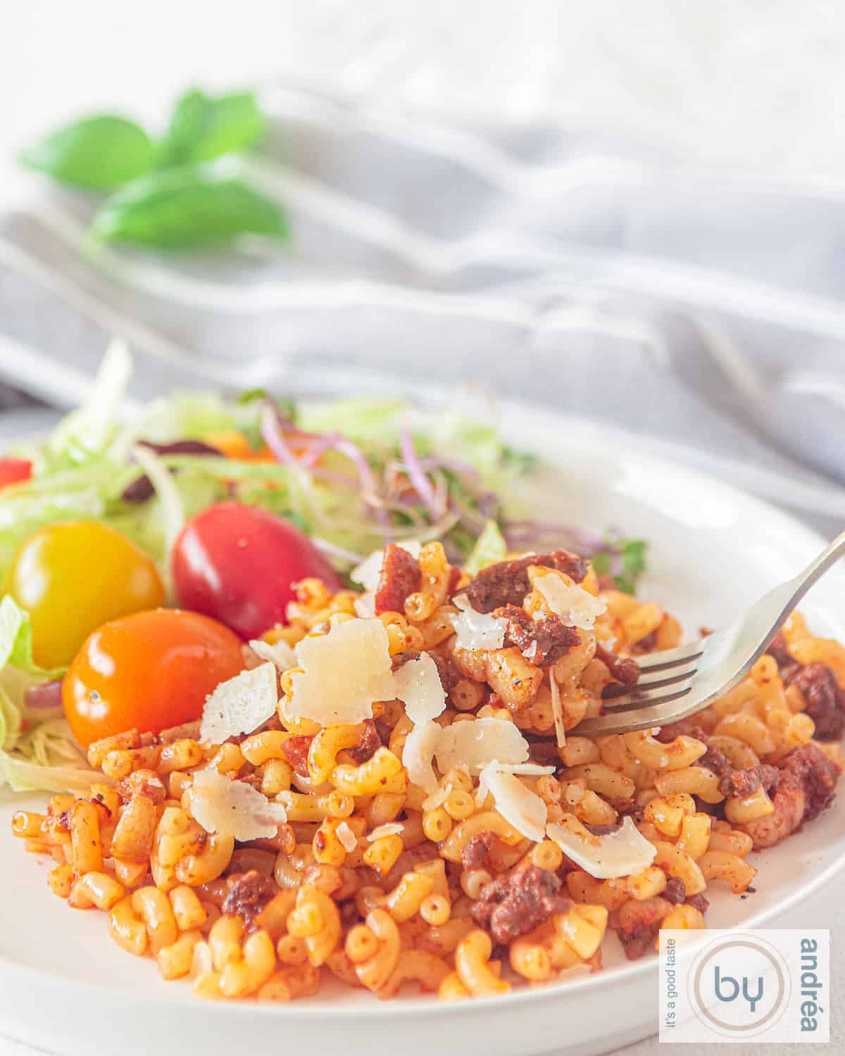 A white plate with macaroni with minced meat, tomato, bacon and grated Parmesan cheese over it.