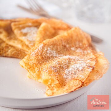 A square picture with crêpes with powdered sugar on top.