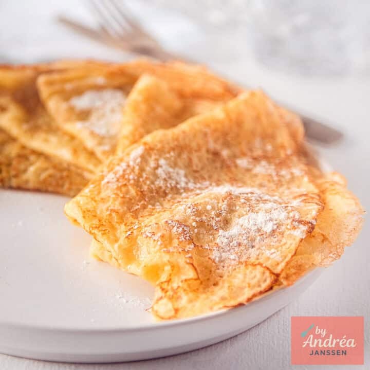 A square picture with crêpes with powdered sugar on top.