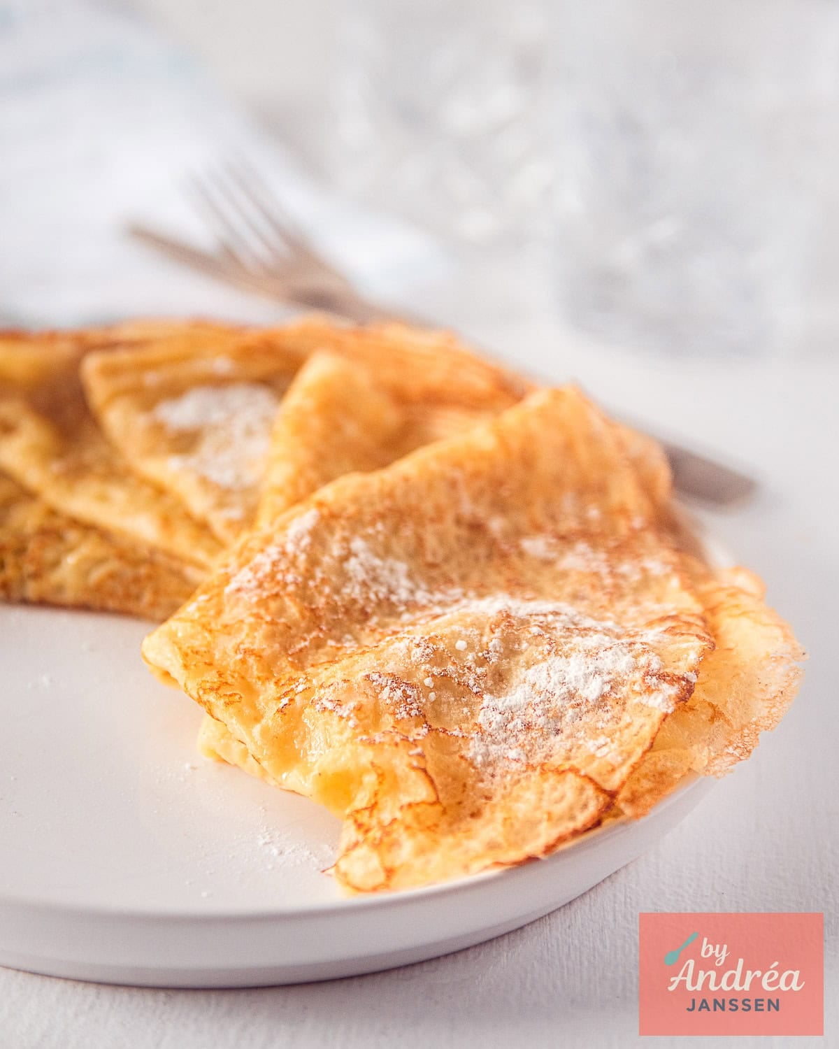 A white plate with crèpes with confectioner's sugar. 