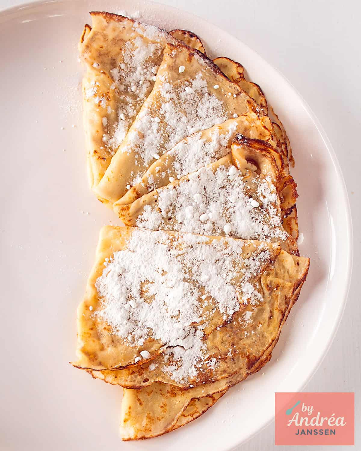Part of a white plate with crêpes (thin pancakes) with confectioner's sugar