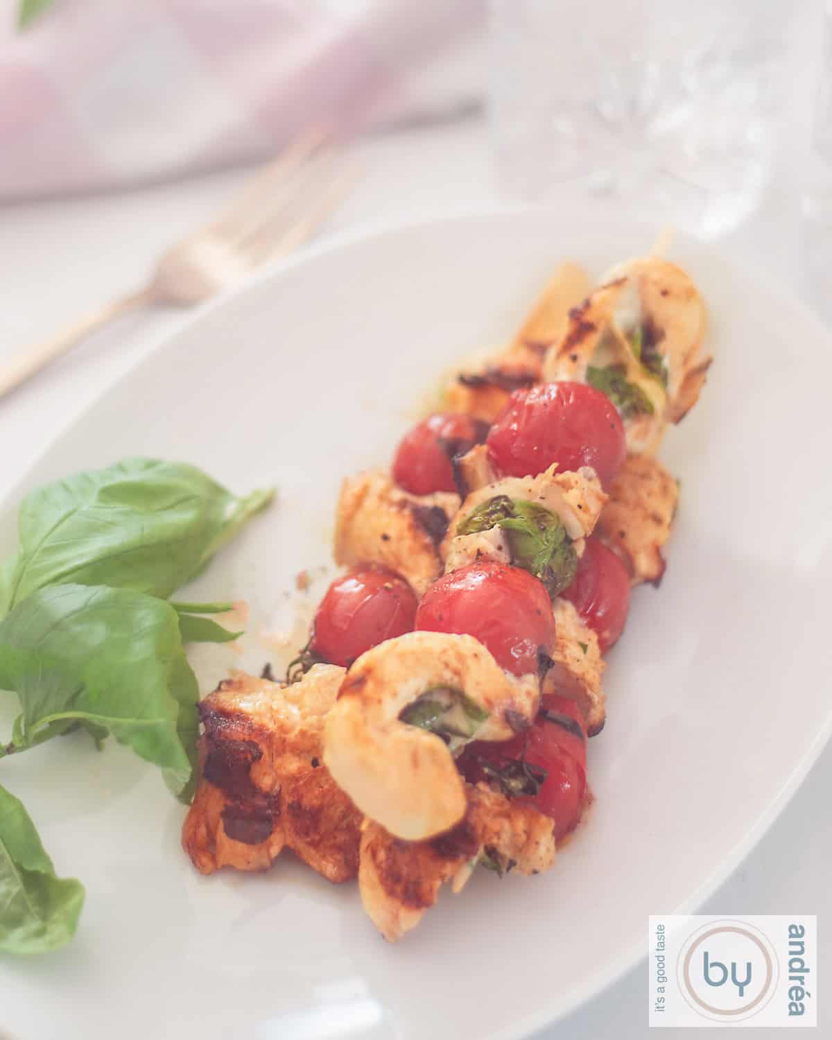 A top-down photo of a platter of three chicken skewers filled with mozzarella and basil with tomatoes.