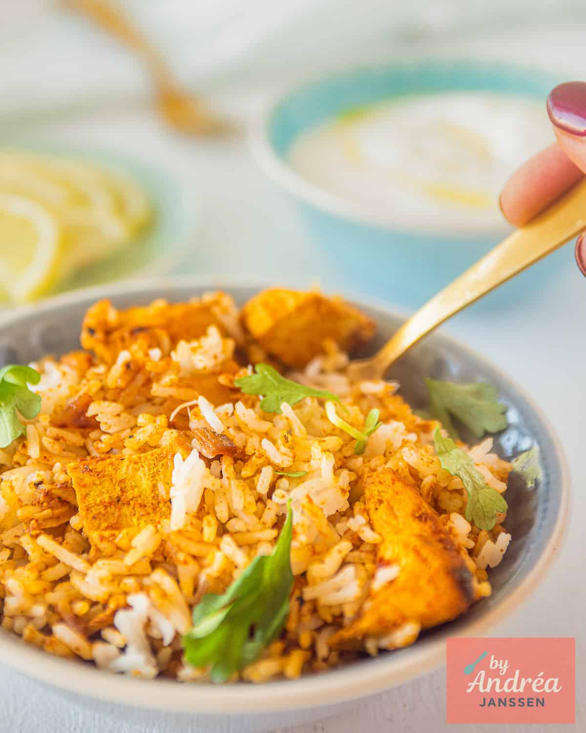 A bowl filled with easy Indian Chicken Tikka biryani. A hand taking a spoon.