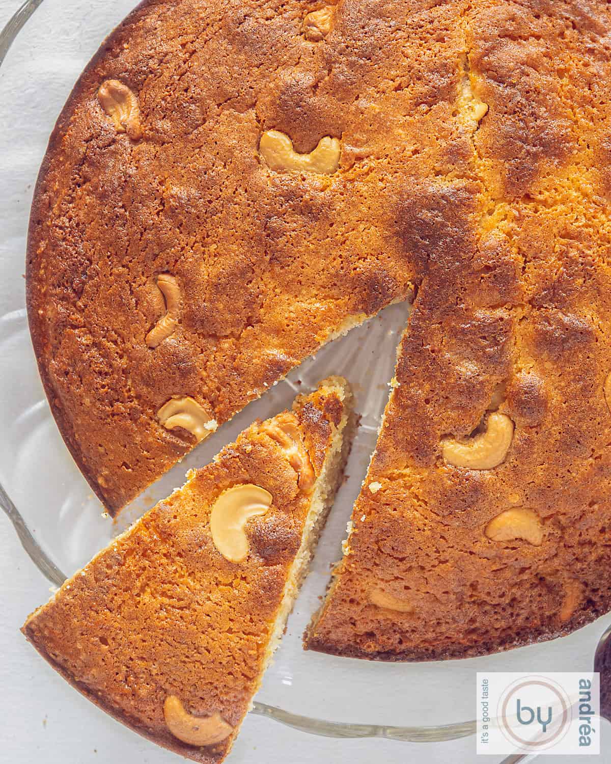 A photo from above of a slice of an Indian Mawa cake with karedamom and cashew nuts. A point cut out.