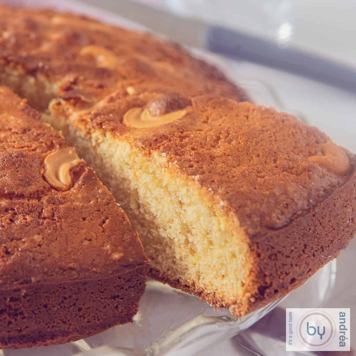 A square photo of a slice of an Indian cake with mawa, cardamom and cashew nuts. A corner cut out.