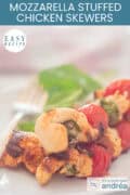 Part of a plate with three skewers of chicken breast, basil, mozzarella, and cherry tomatoes. A caption at the top reads: Easy recipe, Mozzarella-Stuffed Chicken Skewers.