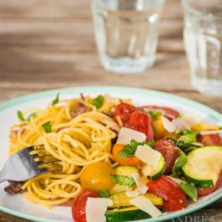 Spaghetti with stir-fried zucchini on a plate and two glasses of water