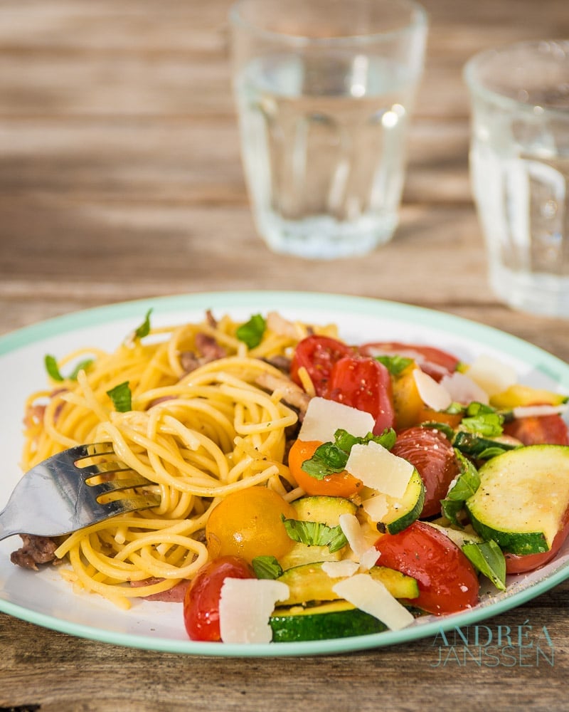 Spaghetti with stir-fried zucchini on a plate and two glasses of water