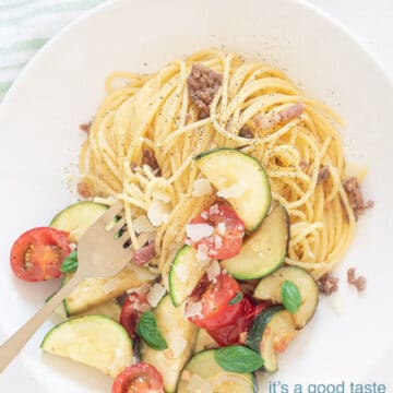 Spaghetti with stir-fried zucchini on a plate and two glasses of water