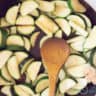 Garlic is added to a frying pan with zucchini slices.