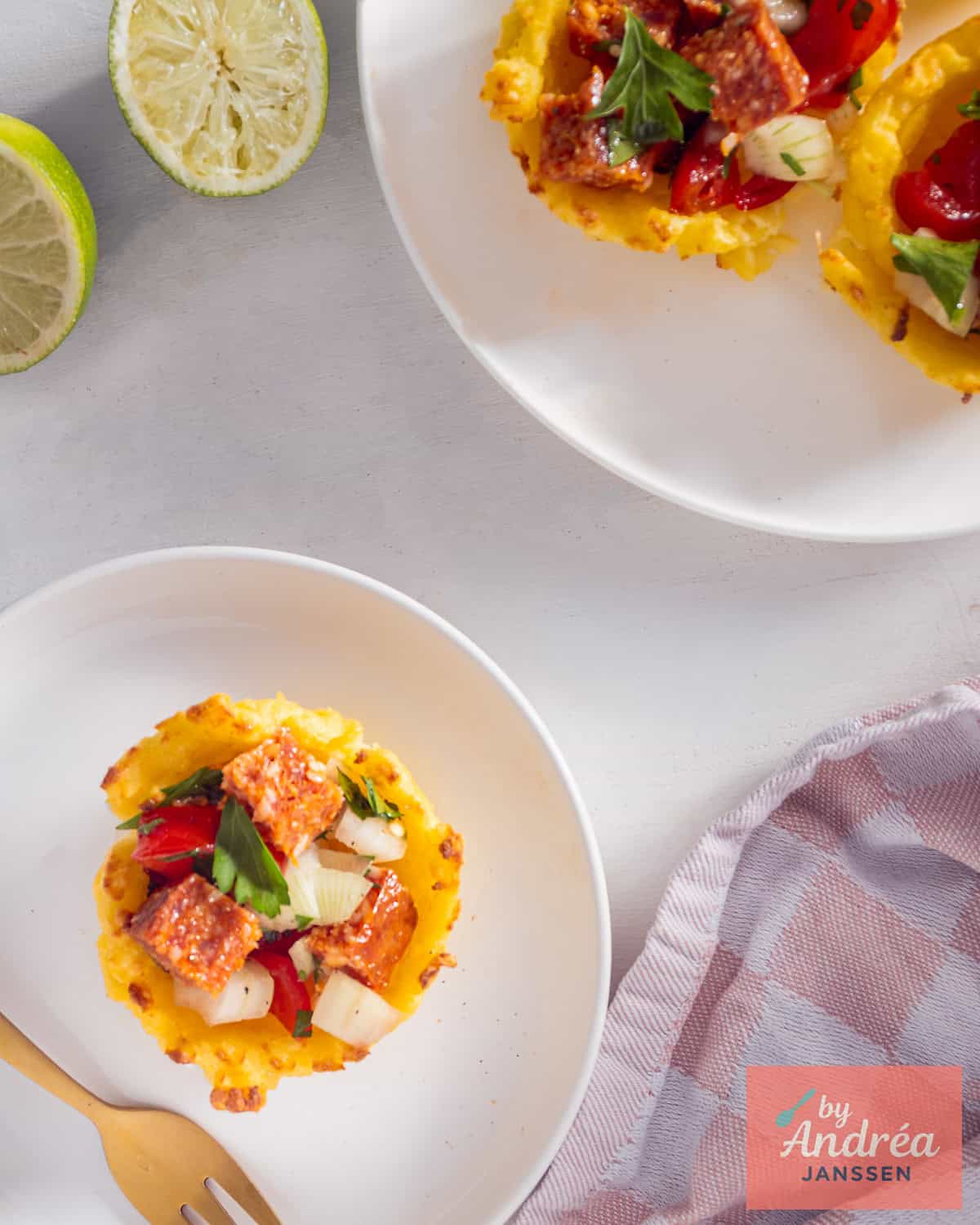 A top down picture with two plates with polenta cups with tomato filling with parsley and onion.