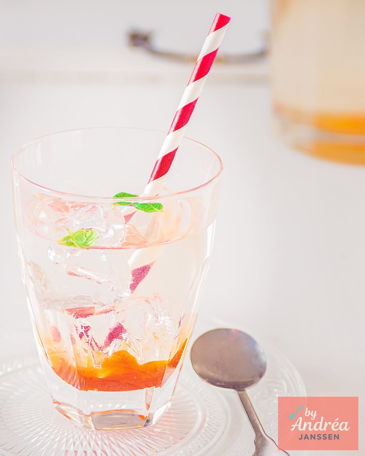 A glass with rosehip syrup, water, and mint on a white background.