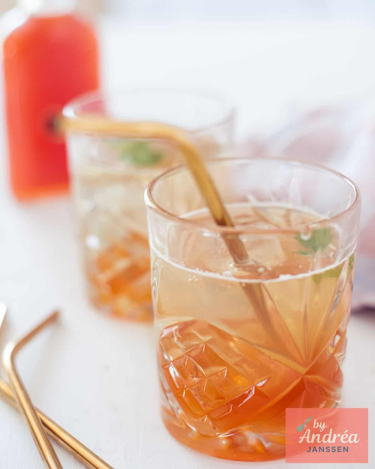 Two glasses filled with rosehip lemonade and a straw, placed diagonally behind each other.
