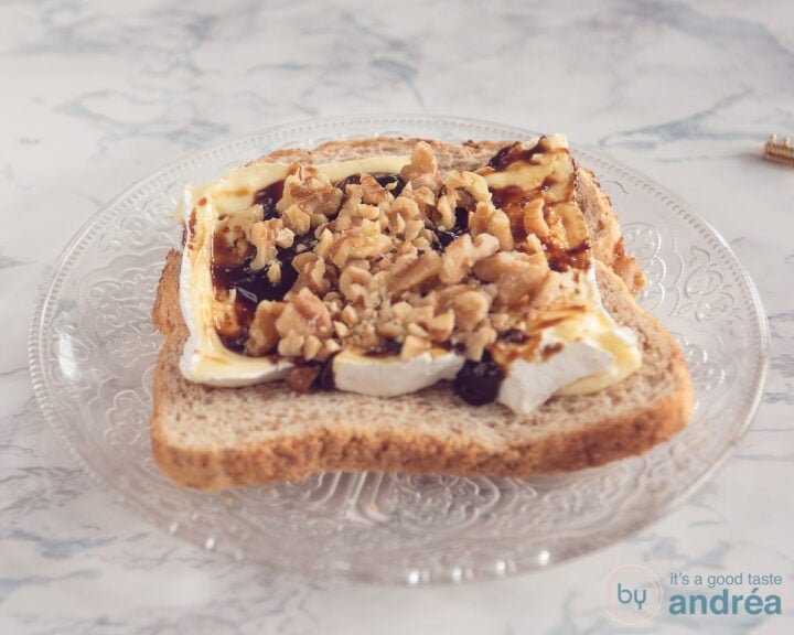 A slice of bread topped with slices of Camembert, apple syrup and walnuts