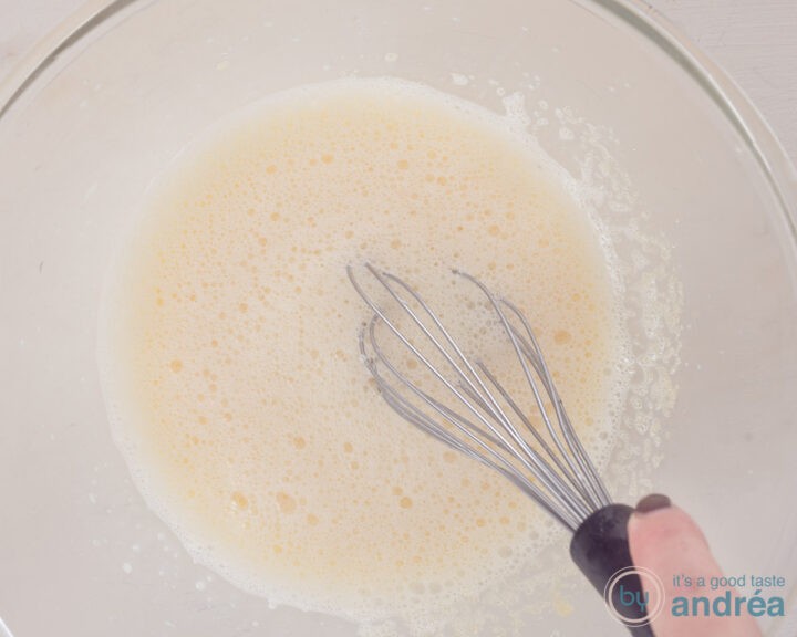The egg yolk is beaten with the sugar in a glass bowl.