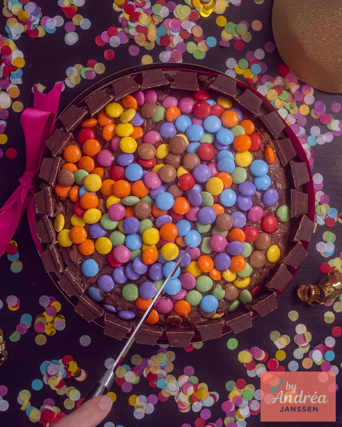 Een foto van bovenaf van een Kitkat smarties taart met daaromheen confetti.