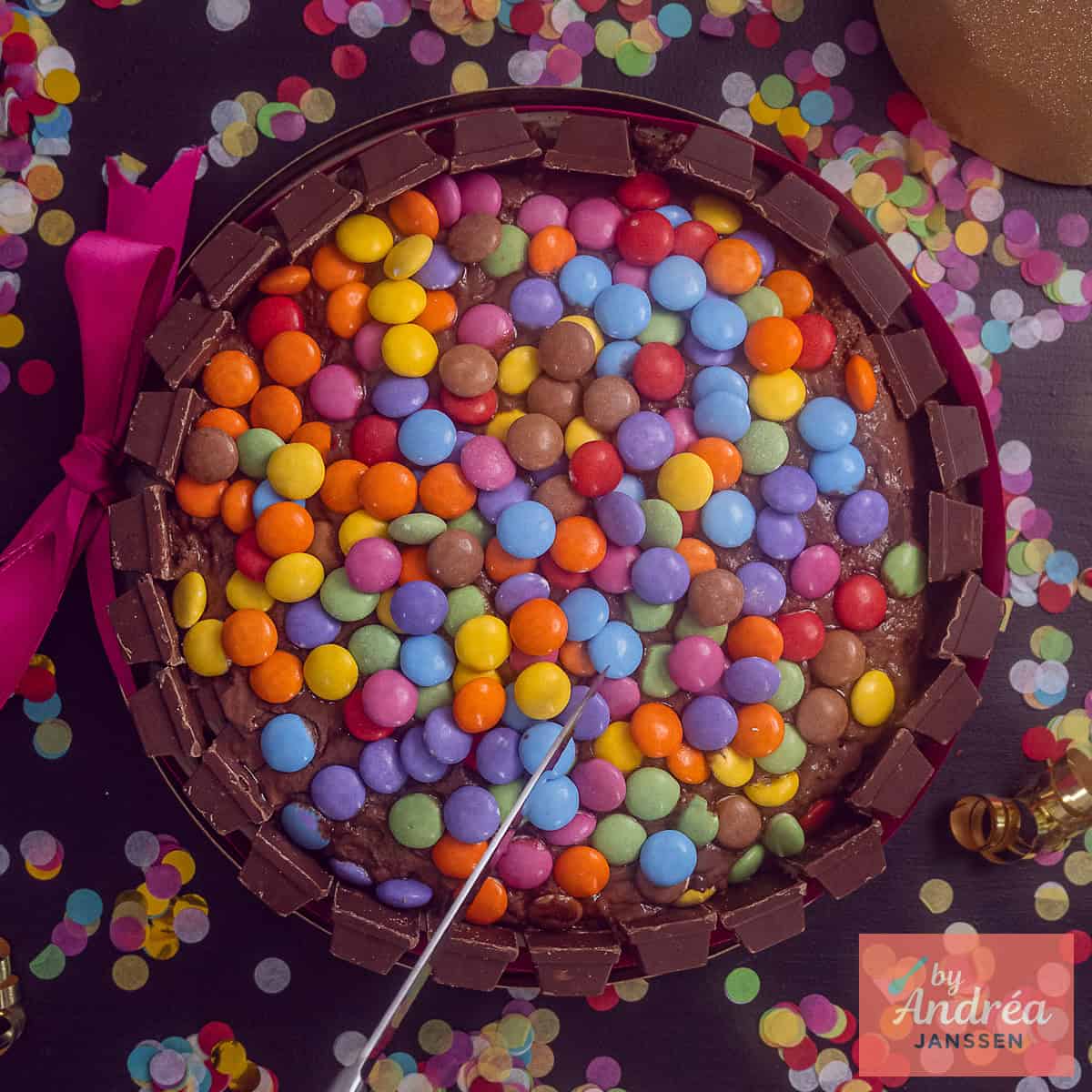 A square photo with a KitKat cake with Smarties and confetti around it.