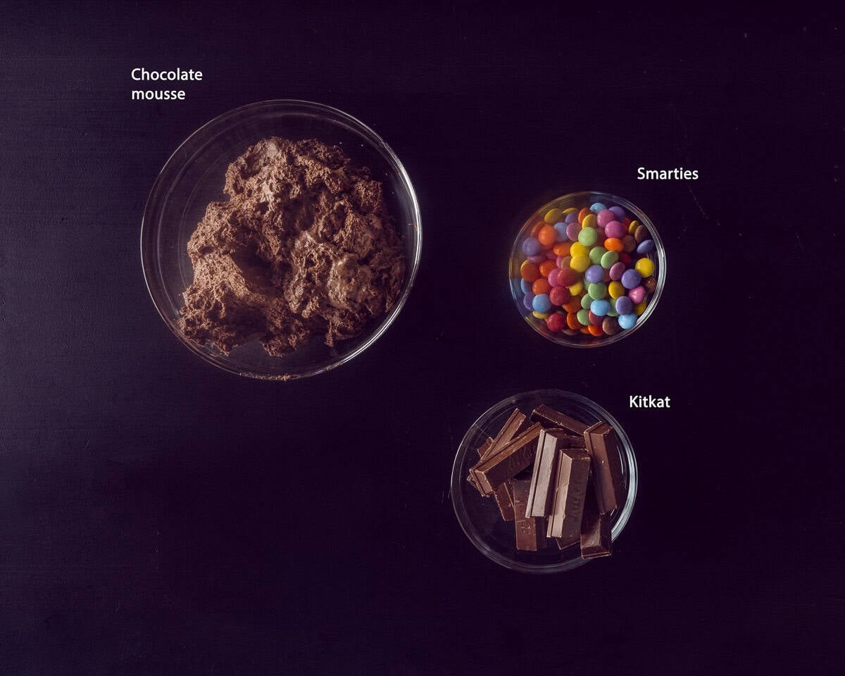 Ingredients topping kit kat smarties cake on a black background with a text description