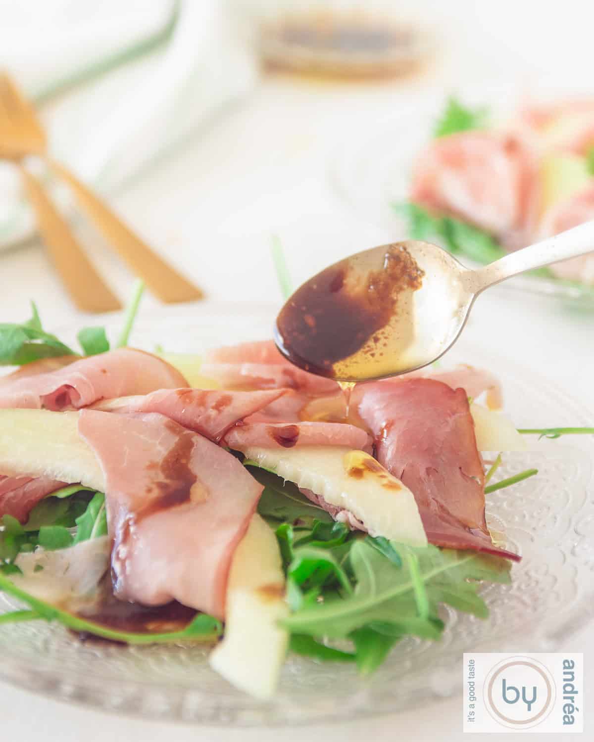A glass bowl with a single-person salad with melon, pancetta, arugula and dressing.