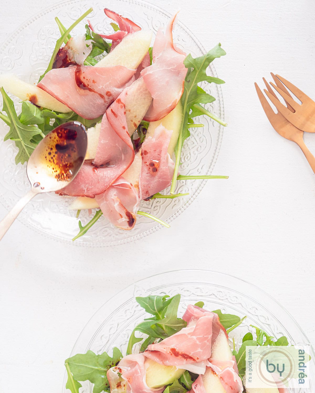 A top-down photo of a glass plate with an Italian salad with melon, pancetta and arugula