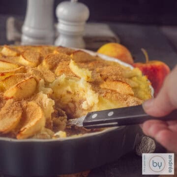 A square photo of part of a casserole with stew, mashed potatoes, apples. A scoop of food is taken out.