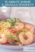 A pink plate with spaghetti, arugula, tomatoes, and shrimp. A text: easy recipe, 15-Minute Shrimp & Arugula Spaghetti
