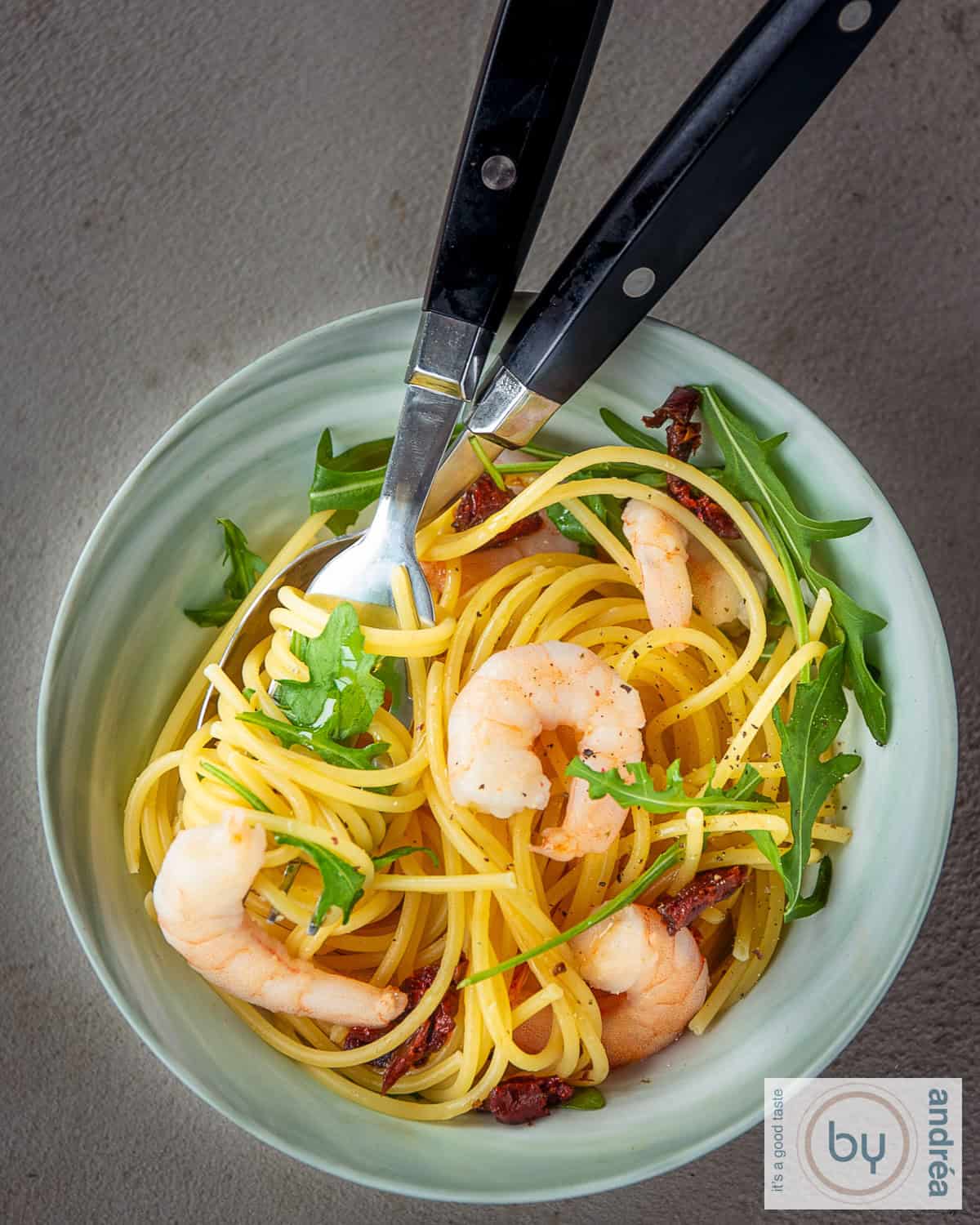 Een foto van bovenaf van een groene schaal met spaghetti, rucola en garnalen